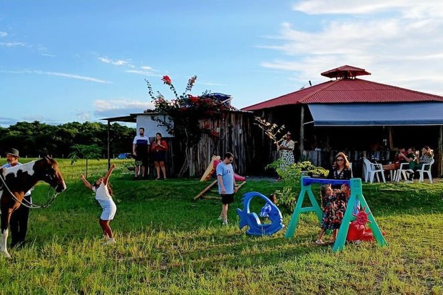 Crianças brincando no balanço e no gramado do Rancho Aroeira ao fim da tarde, com o salão ao fundo