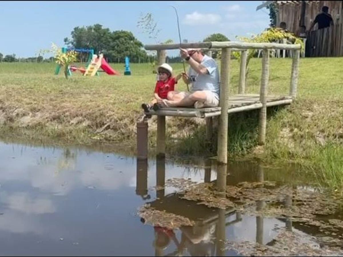 Criança pescando sentada no píer de madeira sobre o lago do Rancho Aroeira